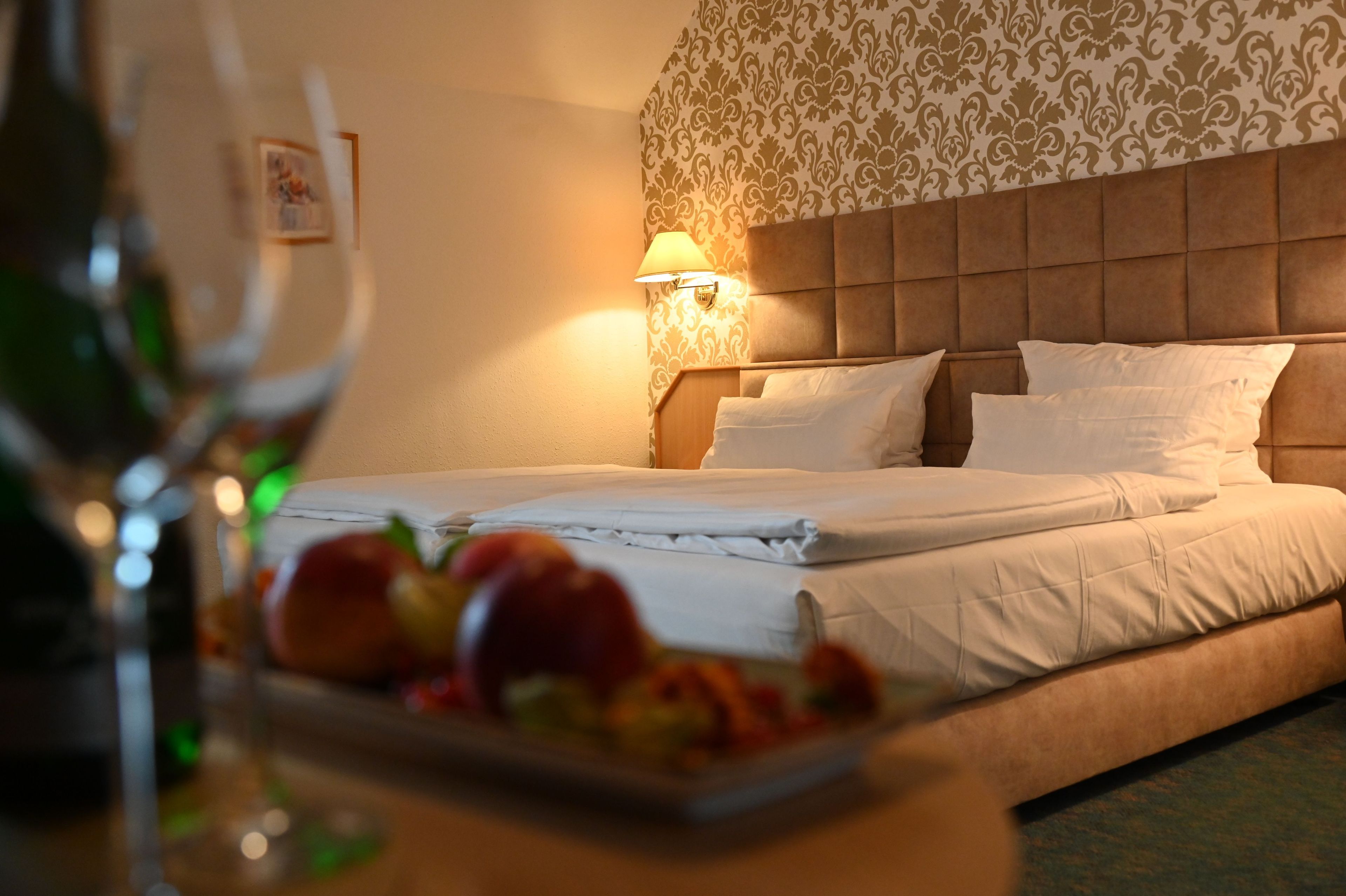 Een hotelkamer met een bed, een wandlamp en een schaal fruit op het nachtkastje.