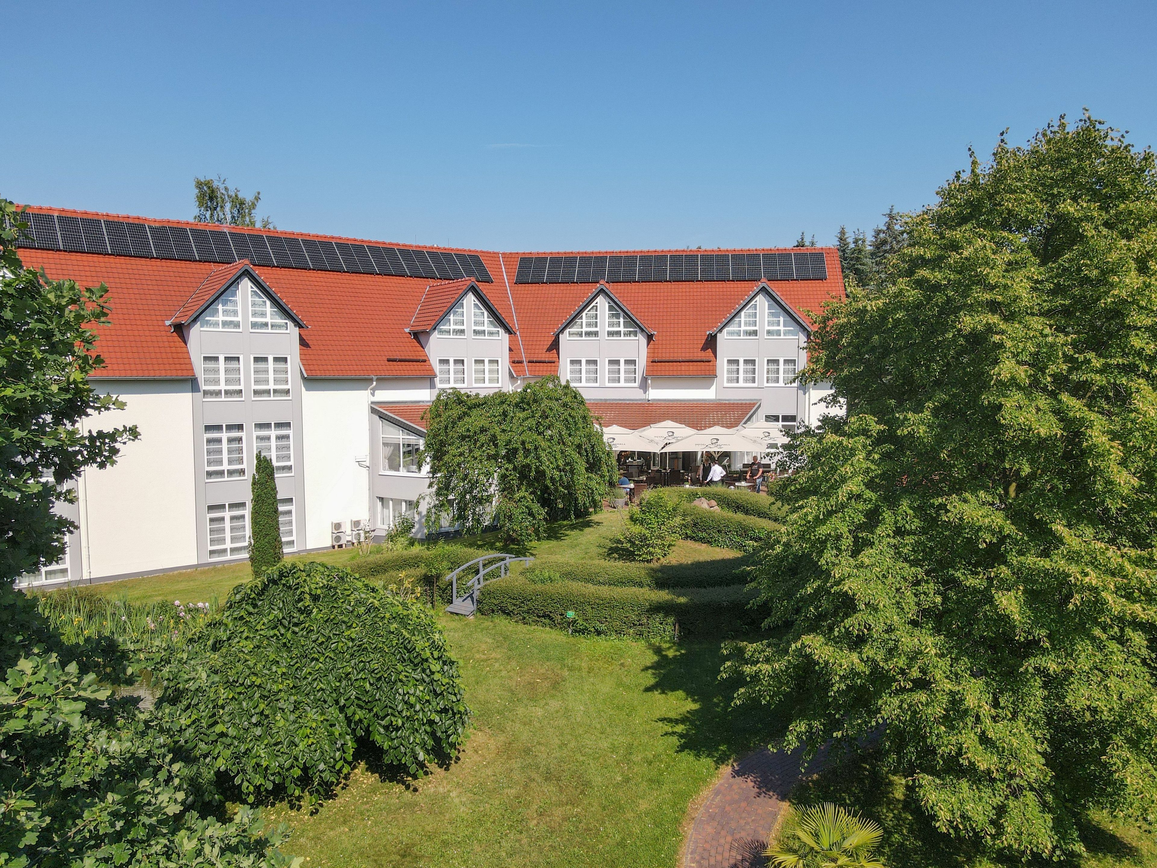 A large building with a red roof, multiple windows, and a well-maintained garden with pathways and trees.