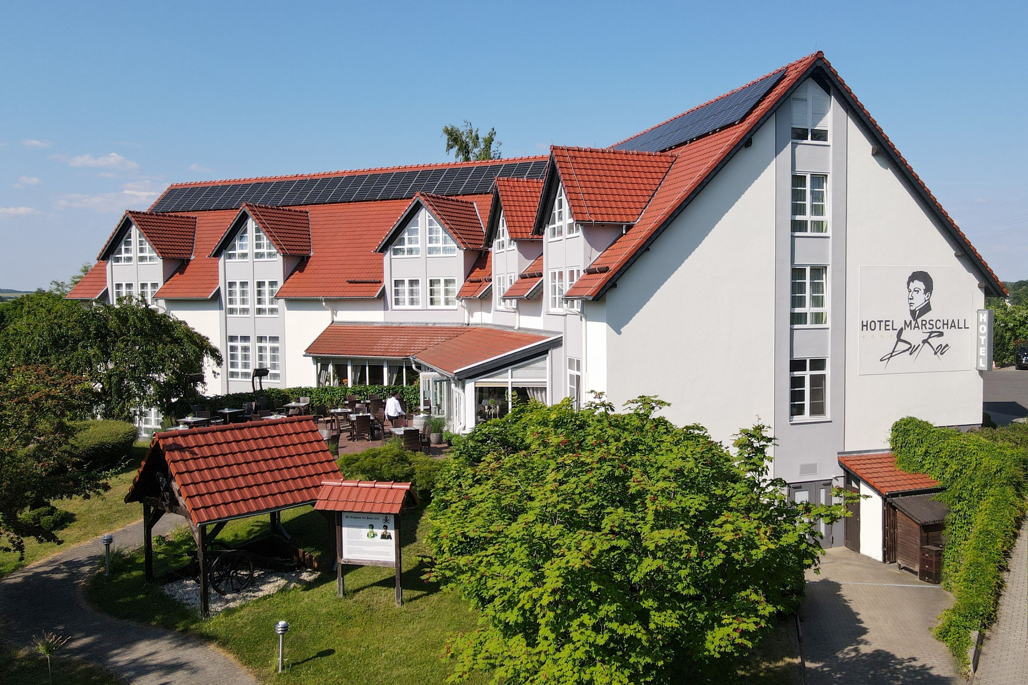 Ein großes Gebäude mit rotem Ziegeldach, zahlreichen Fenstern und einem Schild, das es als Hotel kennzeichnet.