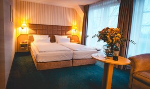 Et hotelværelse med en dobbeltseng, to sengeborde, et lille rundt bord med en flaske og et glas, samt en stol.
