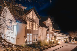Et stort, moderne hotel med flere etager og store vinduer, omgivet af anlagte haver.