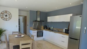 A modern kitchen with a wooden dining table, white cabinets, stainless steel appliances, and a clock on the wall.