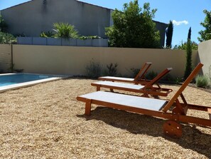 Ett område vid poolen med tre trädäckstolar och en pool.