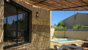 An outdoor patio area with a pool, wicker furniture, and a pergola providing shade.