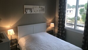 A bedroom with a bed, two bedside lamps, a window with curtains, and a wall-mounted artwork. - House for rent 200 meters from the beach, close to shops. (Saint-Jean-de-Monts)