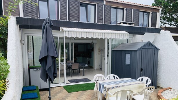 A patio area with a table and chairs, a covered seating area, and a small shed. - House for rent 200 meters from the beach, close to shops. (Saint-Jean-de-Monts)