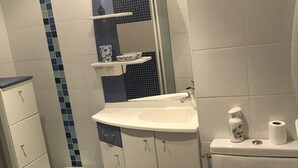A bathroom with a white sink, a mirror, a toilet, and a small trash bin. - House for rent 200 meters from the beach, close to shops. (Saint-Jean-de-Monts)