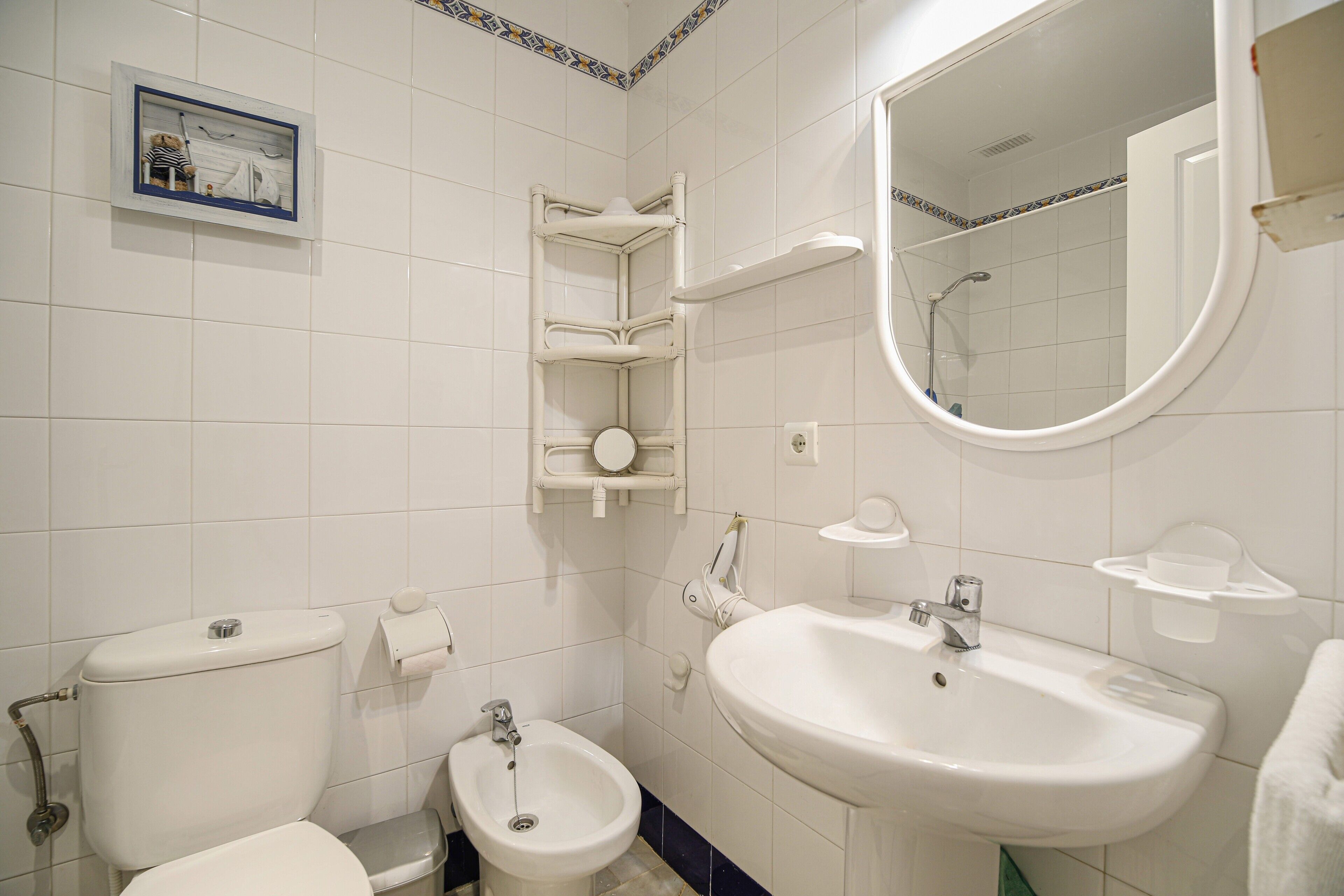 A bathroom with a toilet, bidet, sink, mirror, and a towel rack.