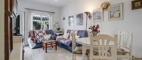 Una sala de estar con sofá, sillas, mesa de comedor y televisor.