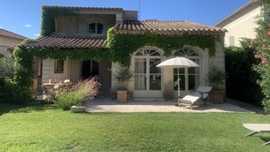A house with a tiled roof, a covered patio with a table and chairs, and a garden with a lawn and shrubs. - Luxury villa in town center; 5* in a quiet location  (Saint-Rémy-de-Provence)