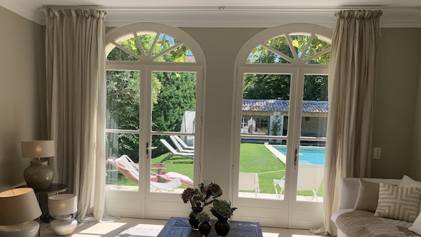 A room with a large arched window, a sofa, a coffee table with a book, and a lamp. - Luxury villa in town center; 5* in a quiet location  (Saint-Rémy-de-Provence)