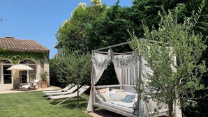 A garden with a canopy bed, lounge chairs, and a house in the background. - Luxury villa in town center; 5* in a quiet location  (Saint-Rémy-de-Provence)