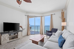 Relax in this stylish living room with a flat-screen TV, sliding glass door to a balcony with ocean views, and comfortable seating areas.