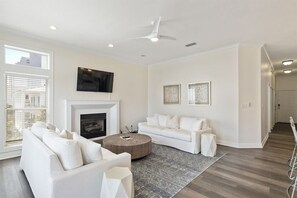 Un salon moderne avec une cheminée, des canapés blancs, une table basse et un ventilateur de plafond.