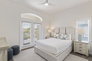 Une chambre à coucher avec un lit, des tables de chevet, un ventilateur de plafond et une vue par la fenêtre.