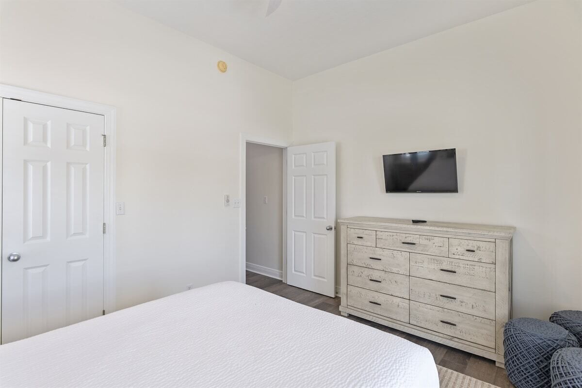 A bedroom with a bed, a dresser, a television, and two doors.