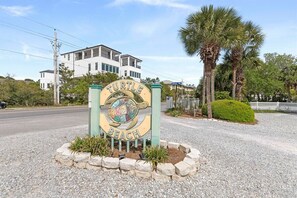 A sign for Turtle Beach with a turtle emblem, surrounded by a gravel area and palm trees.