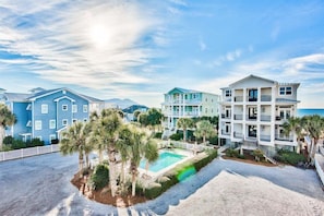A beachfront hotel with multiple-story buildings, a swimming pool, and palm trees.