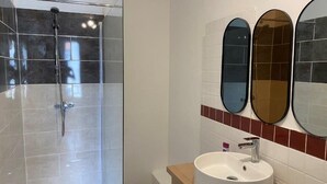 A modern bathroom with a glass-enclosed shower, a sink with a mirror above it, and a tiled wall. - Mansion overlooking the ancient Roman arena (Béziers)