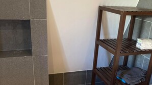 A bathroom with dark tiled walls, a wooden shelf unit, and a white countertop. - Comfortable home near Amsterdam (Zaandam)