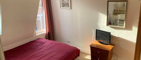 A bedroom with a bed, a desk with a computer, a ceiling fan, a window with curtains, and a framed picture on the wall.
