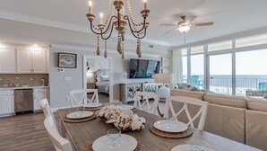 A spacious kitchen with white cabinets, a dining area with a wooden table set for four, and a large window overlooking the ocean. - New Complex!  Lazy River/Slide, Beachfront!  5th Floor (Orange Beach)