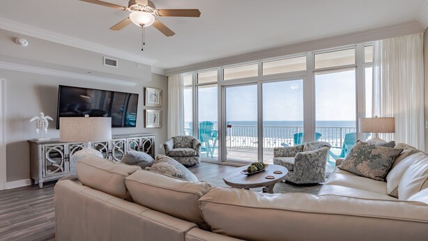 A spacious living room with a large sofa, two armchairs, a coffee table, and a flat-screen TV mounted on the wall. There are large windows offering a view of the beach. - New Complex!  Lazy River/Slide, Beachfront!  5th Floor (Orange Beach)