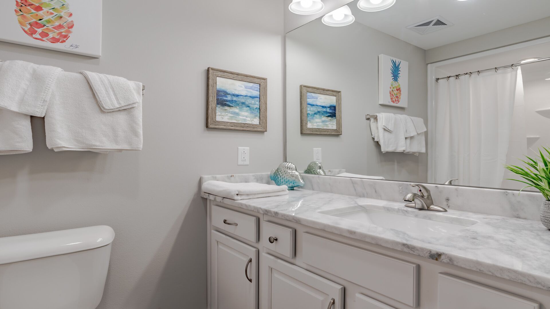 A modern bathroom with a white toilet, a marble sink, and a large mirror. There are towels hanging on the wall and a plant on the counter.