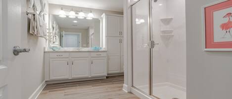 A bathroom with white cabinets, a glass shower enclosure, and a mirror with lights.