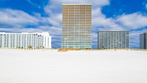 Ett hotell vid stranden med flera våningar, en sandstrand i förgrunden och en klarblå himmel.