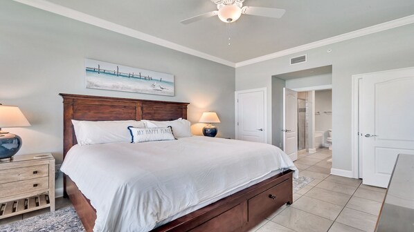 A spacious bedroom with a large bed, bedside tables, a ceiling fan, and a view into the bathroom.
