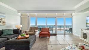 Ein geräumiges Wohnzimmer mit großem Fenster mit Blick auf den Strand, einer Couch, einem Couchtisch und einem Fernseher.