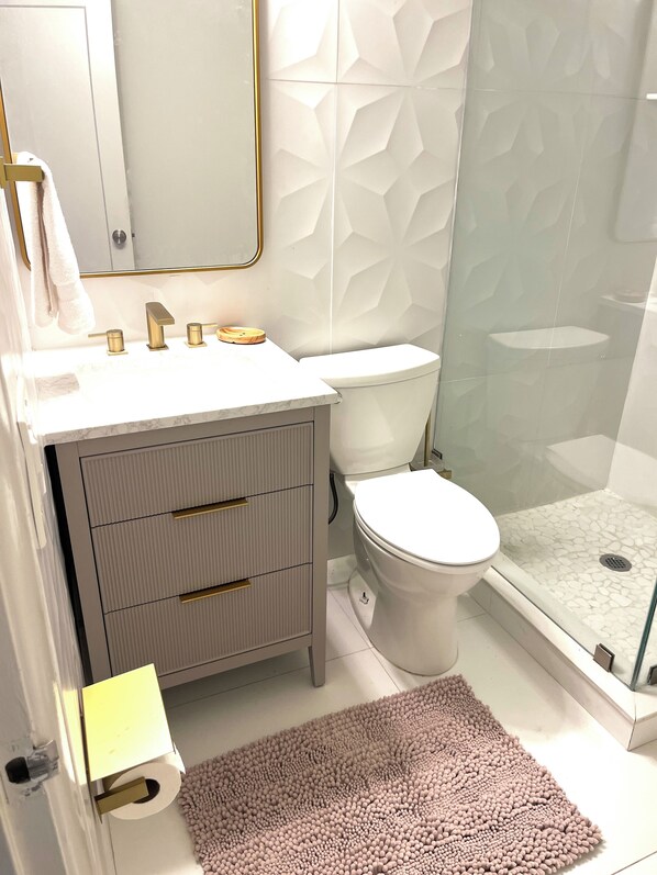 Un baño moderno con tocador blanco, inodoro y cabina de ducha con puertas de vidrio.