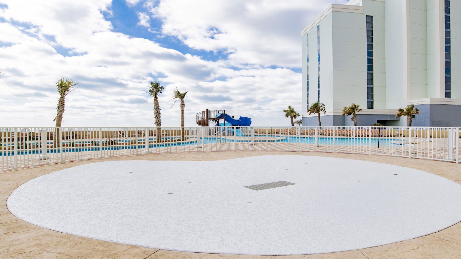 A pool area with a blue slide, palm trees, and a white fence.