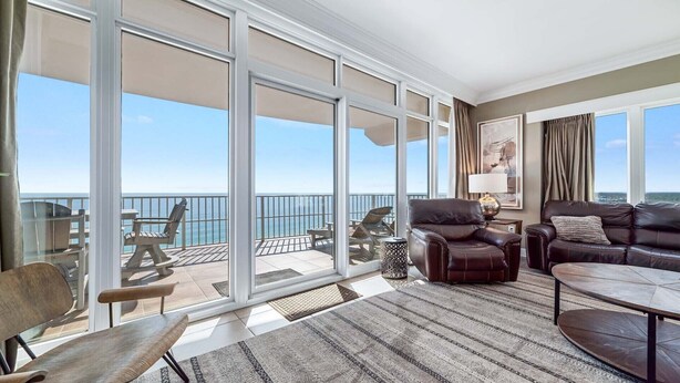 Un'ampia zona giorno con una grande porta vetrata scorrevole che si apre su un balcone con vista sul mare. Si possono vedere un divano in pelle, un tavolino da caffè e una poltrona.