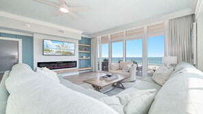 Uma sala de estar espaçosa com uma televisão grande, assentos confortáveis, lareira e varanda com vista para o oceano.