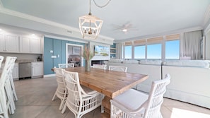 Uma sala de estar ampla com uma mesa de jantar de madeira, cadeiras de vime branco, um sofá e um ventilador de teto.
