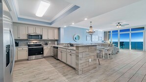 A modern kitchen with a central island, stainless steel appliances, and a view of the ocean through large windows.