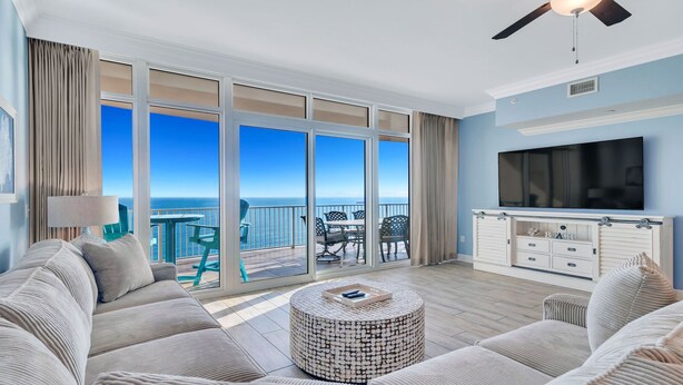 A spacious balcony with a view of the ocean, a sofa set, a round coffee table, and a TV mounted on the wall.