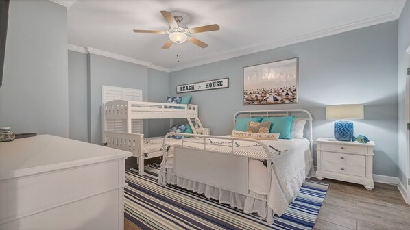 A bedroom with bunk beds, a ceiling fan, a beach-themed wall art, and a bedside table with a lamp.