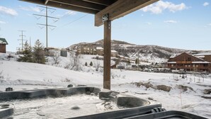 A hot tub area with a wooden structure overhead, a snowy landscape, and a building in the background. - 845 Mill Run Court 5 Bedroom Home by RedAwning (Steamboat Springs)