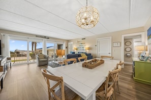 A spacious living area with a dining table, chairs, a sofa, and a chandelier. - Spotted Sandpiper Condo Easy access to Pier, Pool and Beach Access are Steps Away by RedAwning (Fernandina Beach)