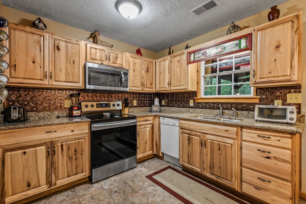 A kitchen with wooden cabinets, a microwave, stove, dishwasher, and a window with a stained glass design.