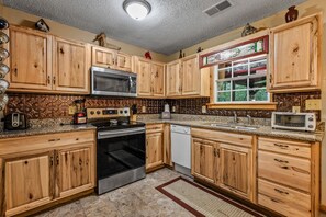 A kitchen with wooden cabinets, a microwave, stove, dishwasher, and a window with a stained glass design.