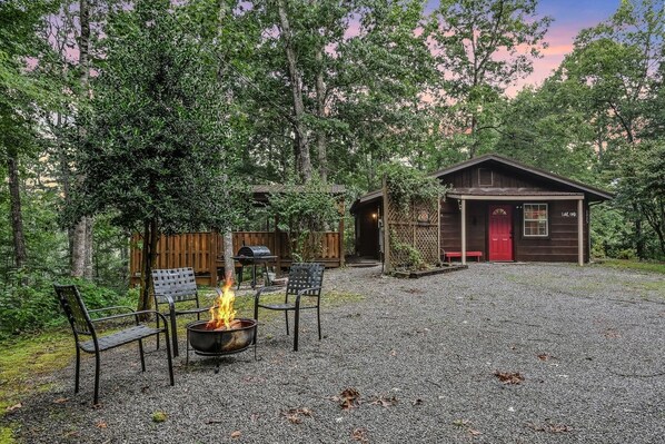 A rustic cabin with a gravel driveway, a fire pit, and outdoor seating.