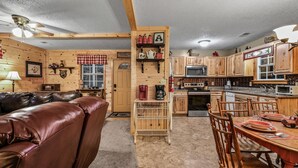 Interior acogedor de una cabaña con un sofá de cuero, una mesa de comedor de madera y una zona de cocina.