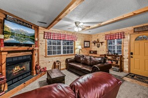 A cozy log cabin interior with a fireplace, leather furniture, and a television mounted above it.