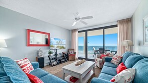 A spacious living room with a large blue sofa set, a coffee table, and a view of the ocean through large windows. - Windward Pointe 502-Beachfront 3bd/2ba-Sleeps 8-Heart of Orange Beach (Orange Beach)