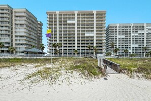 A beachfront hotel with multiple floors, a flag, and a beach access point.