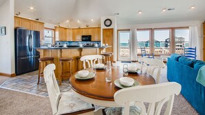 A spacious kitchen with wooden cabinets, a black refrigerator, and a dining area with a round table and white chairs. - Premier Semi-Oceanfront w/ Pool, Hot Tub, Elevator, Theater, Bocce/Putting Court (Rodanthe)